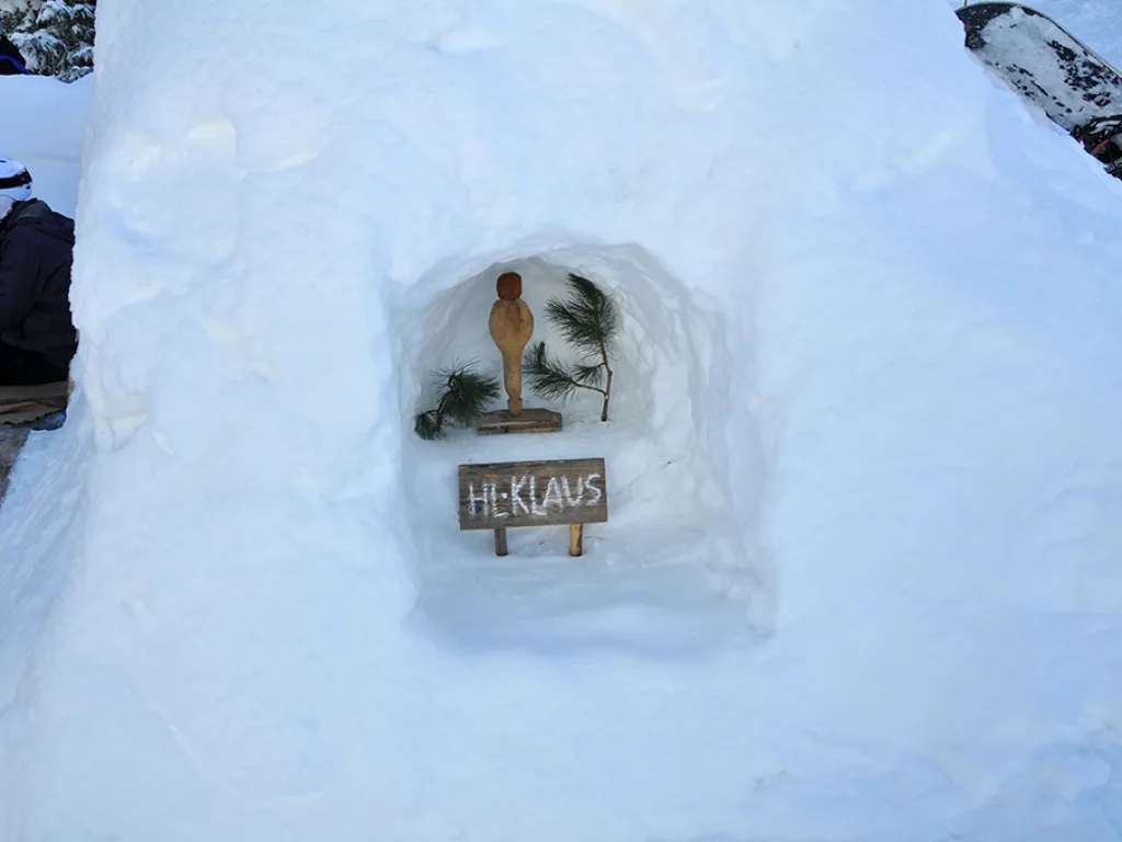 Kleine Figur mit Schild „Hl. Klaus“ in einer Schneenische.